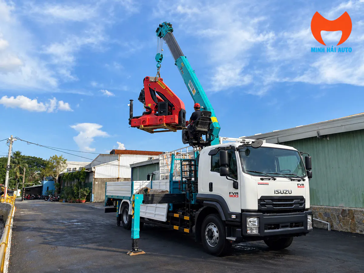 Xe tải gắn cẩu ống lồng đã bung chân chống đang nâng một cẩu gập khúc màu đỏ đặt trên pallet gỗ tại xưởng