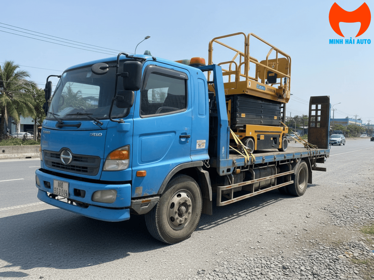 Công nhân đang đứng trên sàn thao tác của xe nâng người cắt kéo điện để lắp đặt hoặc bảo trì hệ thống điện, PCCC trên trần một nhà xưởng.