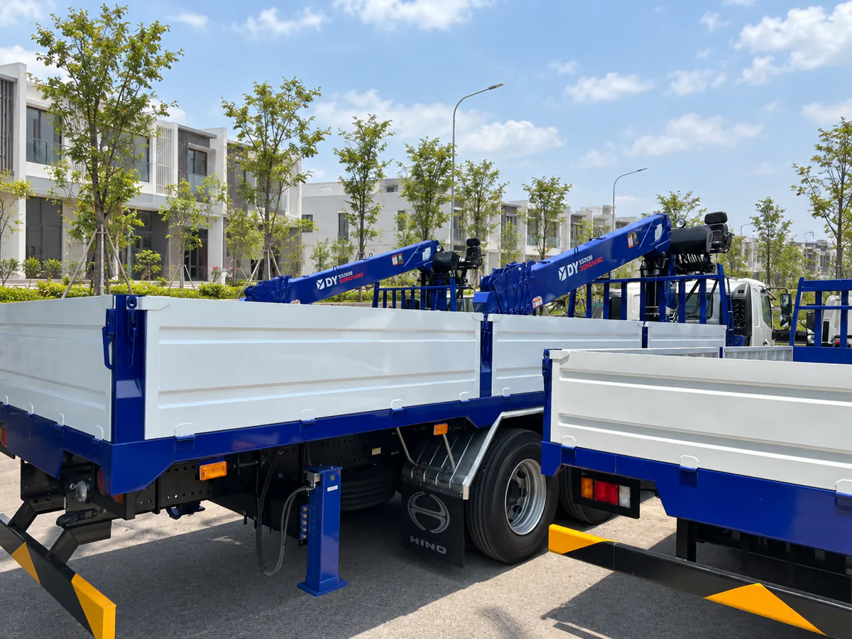 Các xe tải thùng lửng trắng khung xanh với cẩu Dongyang trong khung cảnh đô thị