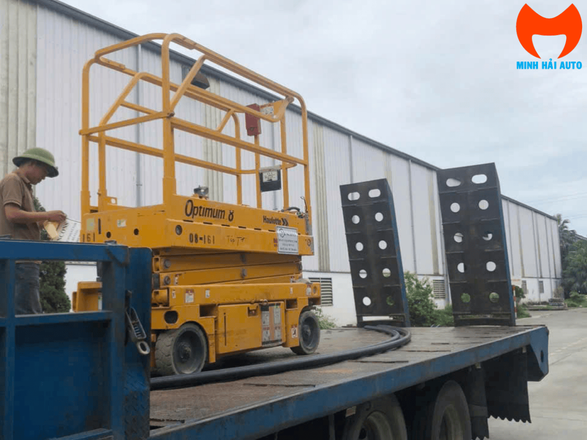 Một chiếc xe nâng người cắt kéo địa hình (động cơ diesel) đang hoạt động trên công trường xây dựng, giúp công nhân tiếp cận mặt ngoài của tòa nhà.