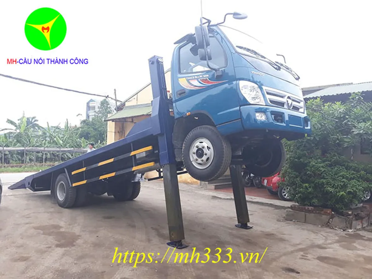 Xe nâng đầu Thaco Ollin 700C màu xanh đang nâng đầu trên chân chống thủy lực, sàn chở máy nghiêng xuống mặt đất