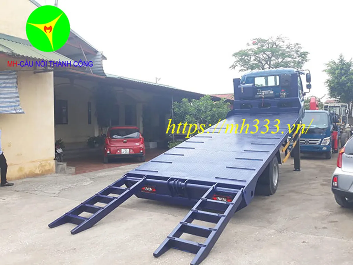 Sàn chở máy Thaco Ollin 700C nghiêng với hai cầu dẫn gập đã hạ xuống mặt sân