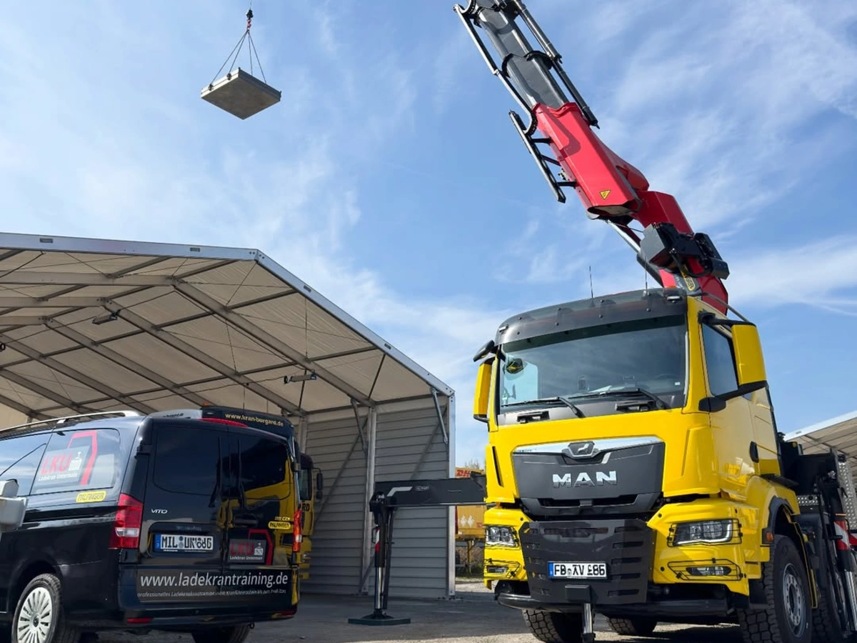 Xe MAN màu vàng gắn cẩu Palfinger nâng kiện hàng lên cao trong sân