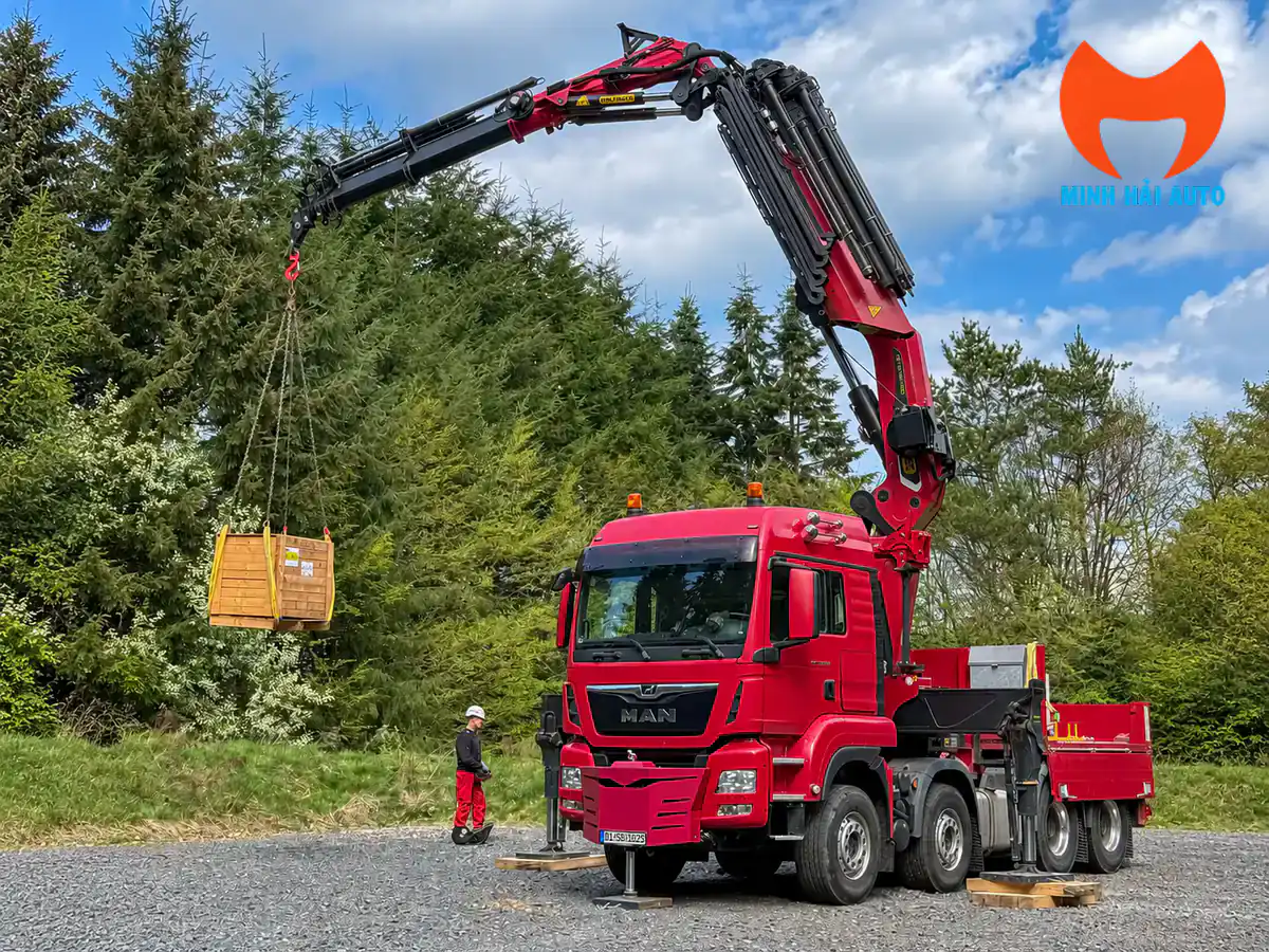 Xe MAN đỏ gắn cẩu gập Palfinger nâng kiện gỗ tại khu vực ngoài trời