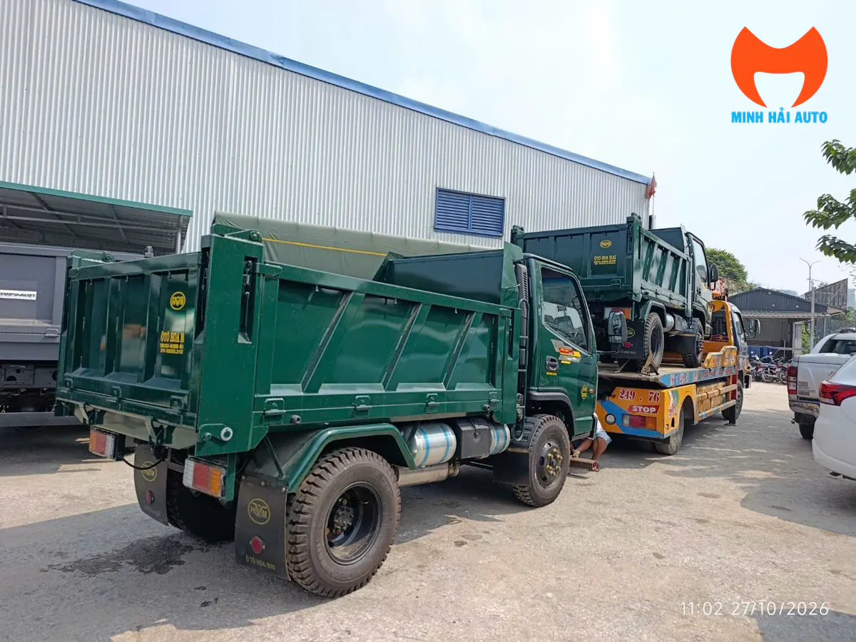 Xe tải ben Hoa Mai đỗ trên sân bãi phía sau xe chở chuyên dùng đang cõng một xe ben Hoa Mai khác