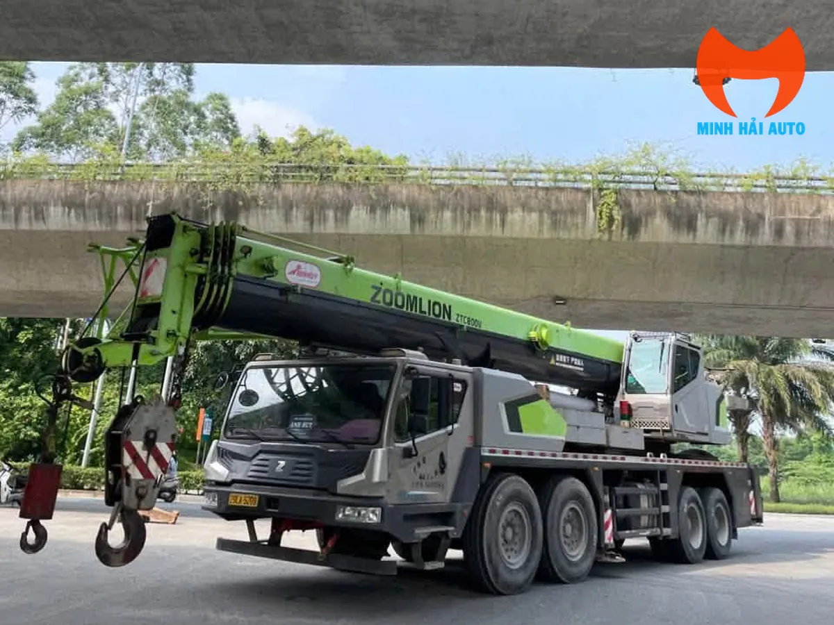 Xe cẩu bánh lốp Zoomlion nhìn từ phía trước bên trái, đỗ dưới gầm cầu vượt, cần thu gọn dọc thân xe, móc cẩu ở phía đầu xe