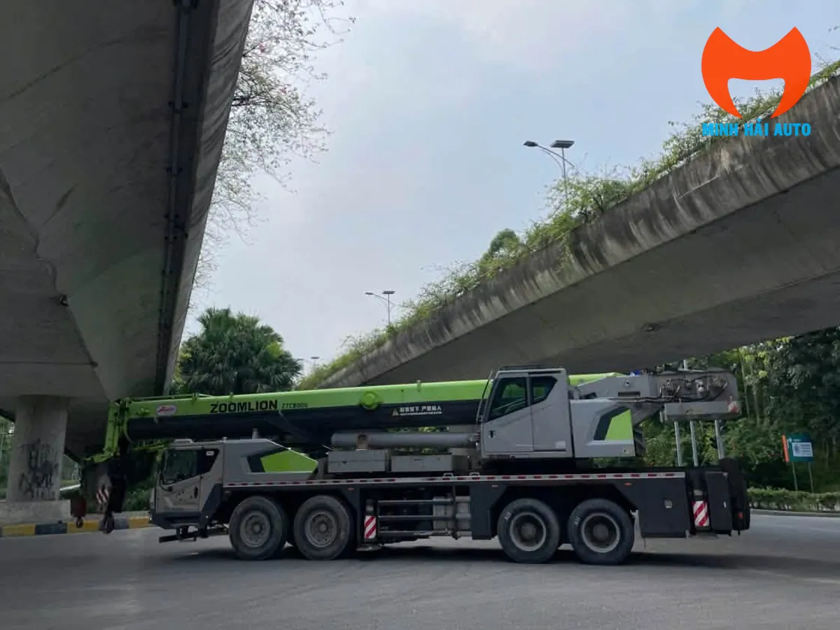 Xe cẩu bánh lốp Zoomlion nhìn ngang toàn thân, đỗ dưới gầm cầu vượt có mặt dưới nghiêng về phía cột trụ