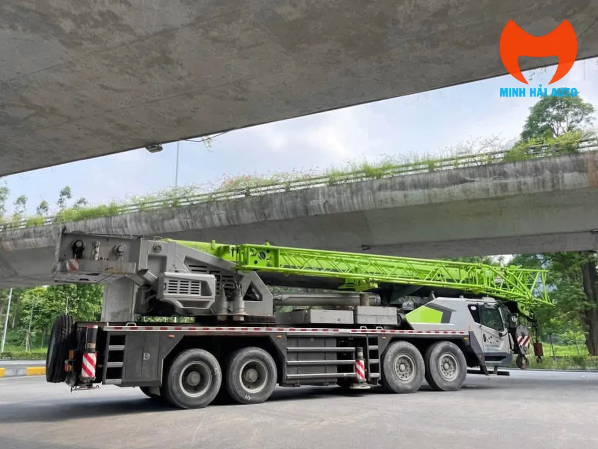 Xe cẩu bánh lốp Zoomlion nhìn từ phía sau bên trái, cần dạng giàn thu gọn trên thân xe, đỗ dưới gầm cầu vượt