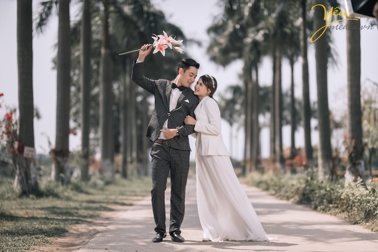 cô dâu chú rể đi dạo bên hàng cây dưới trời nắng