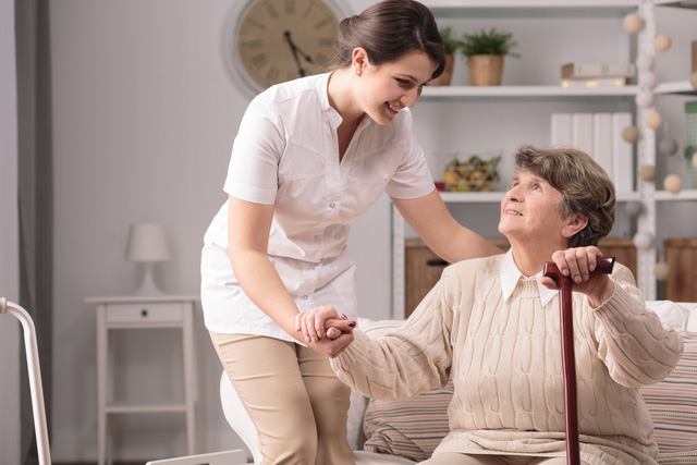 Nhân viên chăm sóc hỗ trợ người cao tuổi cầm gậy trong phòng khách