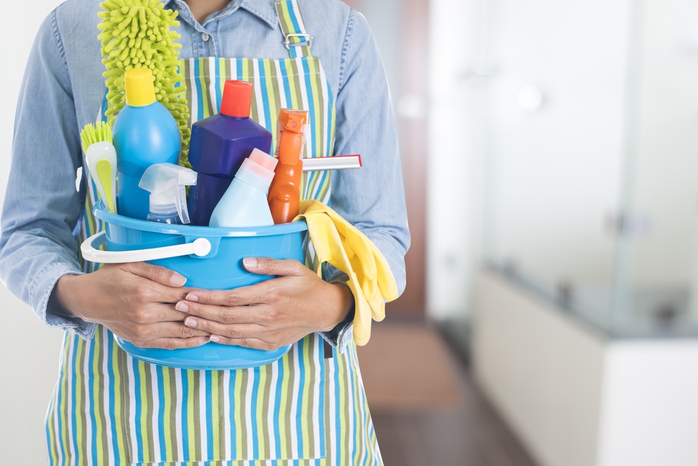 Người mặc tạp dề cầm xô đựng dụng cụ và chất tẩy rửa