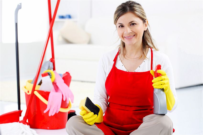Người giúp việc mặc tạp dề đỏ đang lau dọn nhà bằng các dụng cụ vệ sinh.