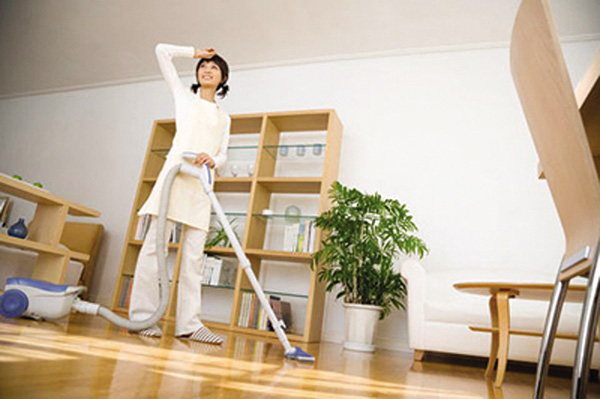 Người giúp việc đang dùng máy hút bụi dọn dẹp phòng khách
