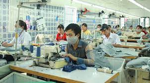 Công nhân đeo khẩu trang làm việc tại xưởng may với máy móc và vải