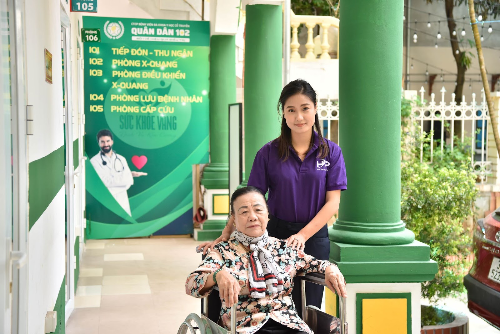 Nhân viên chăm sóc hỗ trợ người cao tuổi ngồi xe lăn trước cơ sở y tế