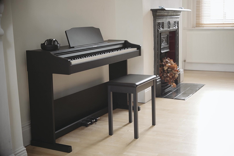 Roland rp102 electric piano built against the wall, with a seat in front