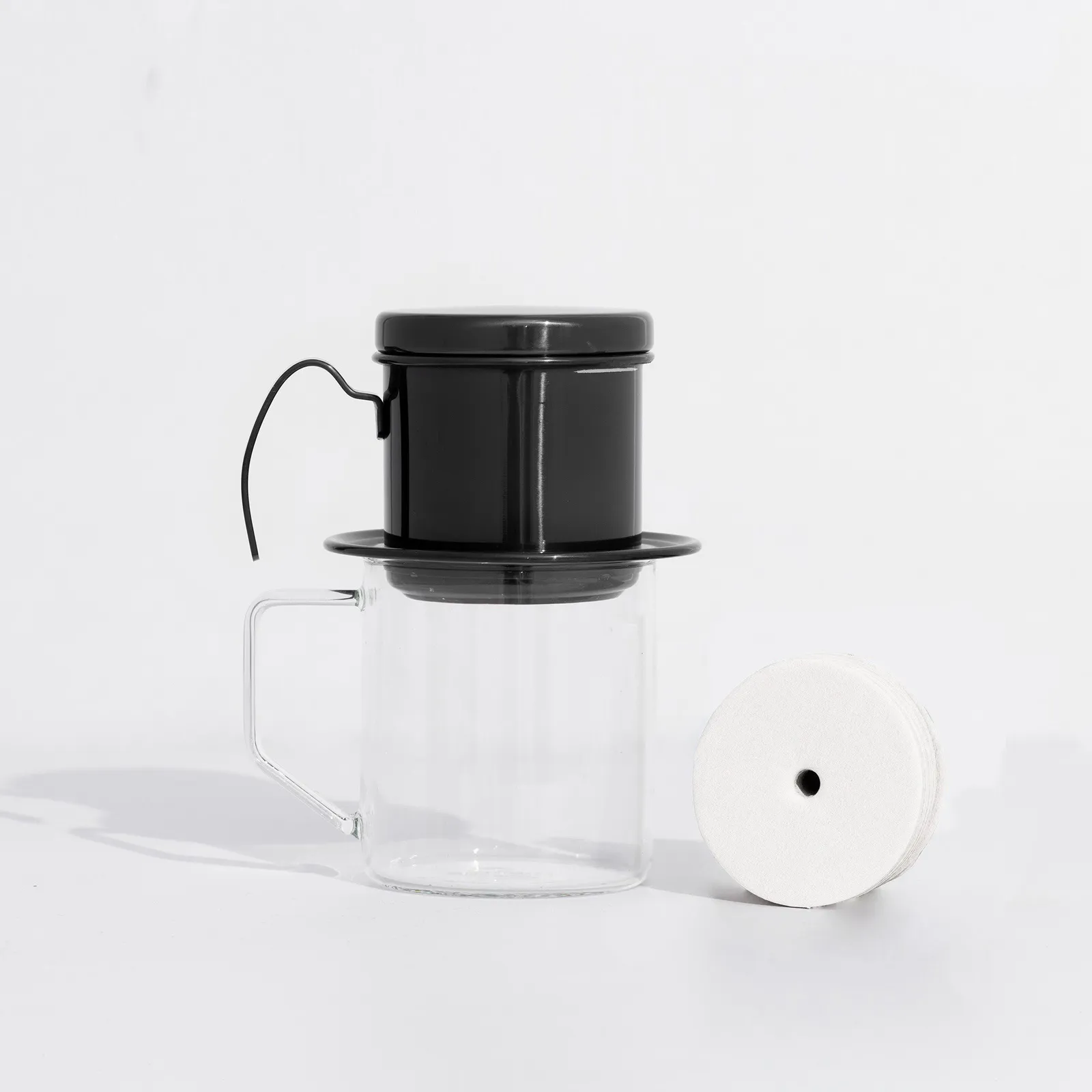 Bộ combo pha phin gồm phin inox màu đen đặt trên ly thuỷ tinh và tờ giấy lọc tròn