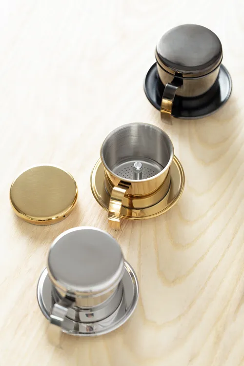 Ba nắp phin cà phê inox màu gold bạc và đen đặt trên mặt gỗ
