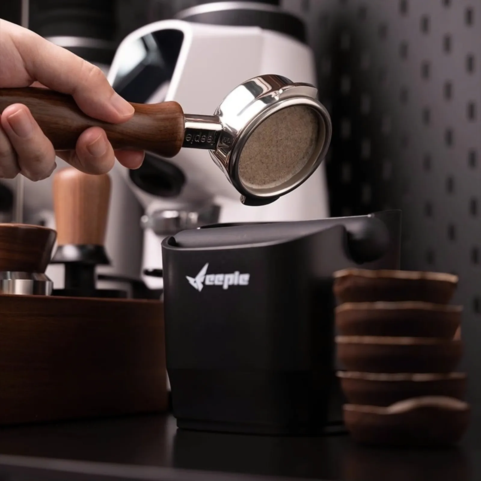 Tay cầm portafilter gõ bã cà phê vào hộp đập bã màu đen trên bàn pha chế