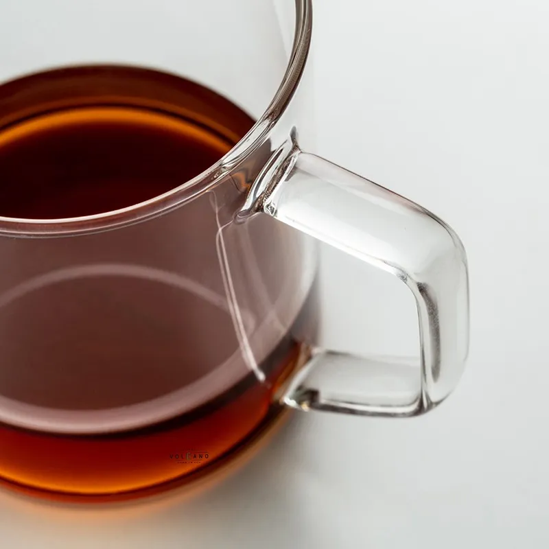 Cận cảnh ly thuỷ tinh trong suốt chứa đầy cà phê màu nâu đỏ nhìn rõ qua thành ly