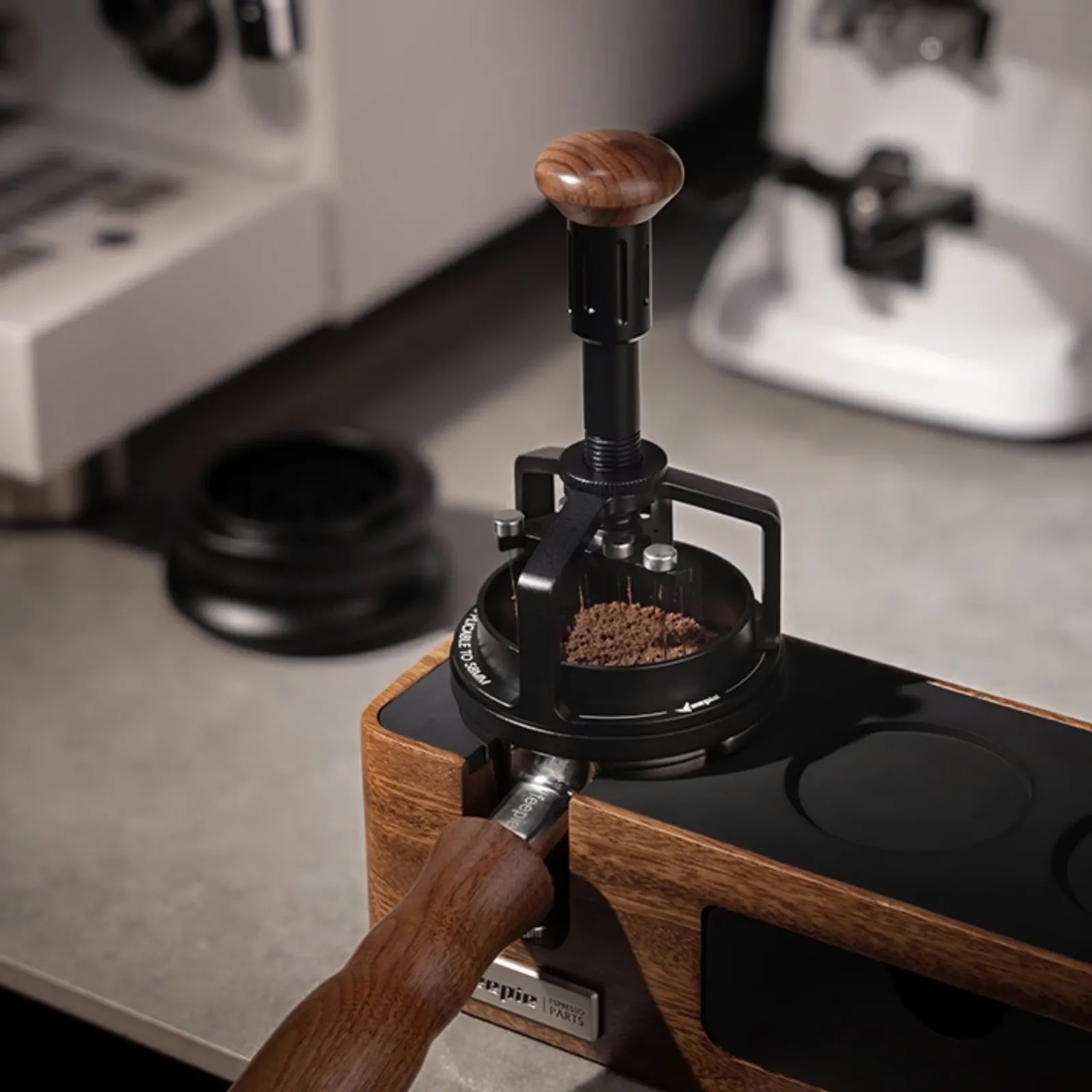 Kim xoay Feepie Wood Charm đang tán bột trong tay cầm portafilter đặt trên giá gỗ