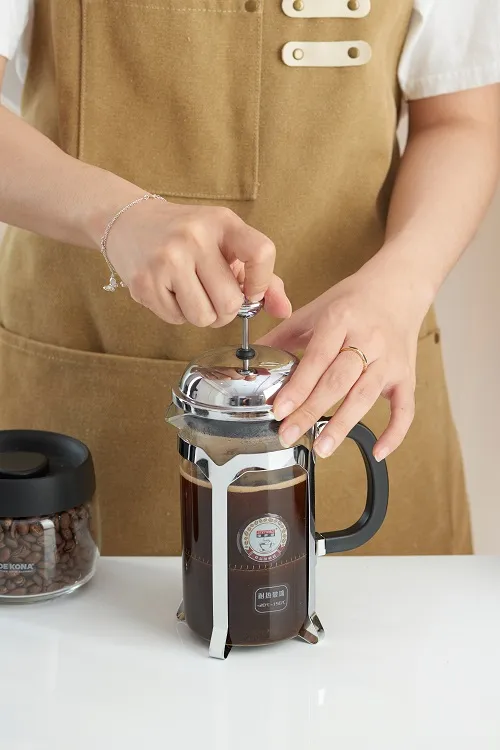 Bàn tay ấn piston lưới lọc xuống trong bình French Press đã pha xong