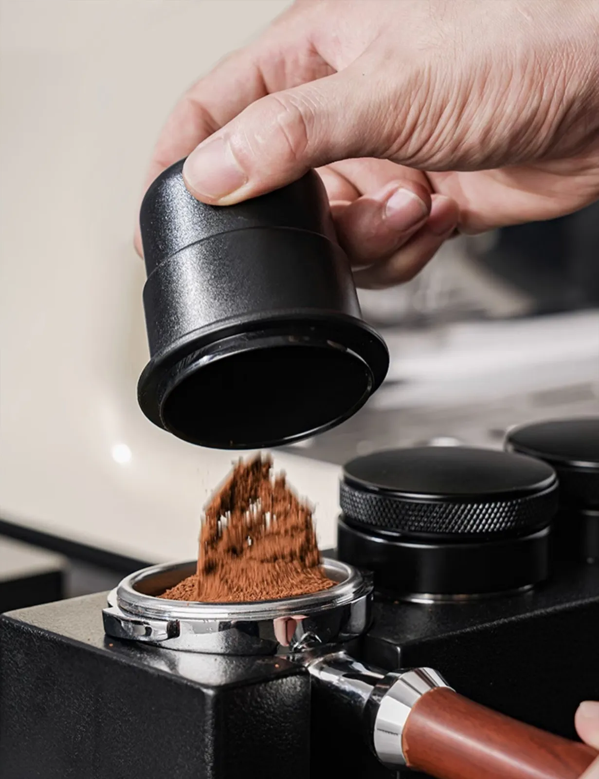 Tay đang cầm ly dosing cup màu đen đổ bột cà phê xay vào giỏ lọc tay cầm espresso