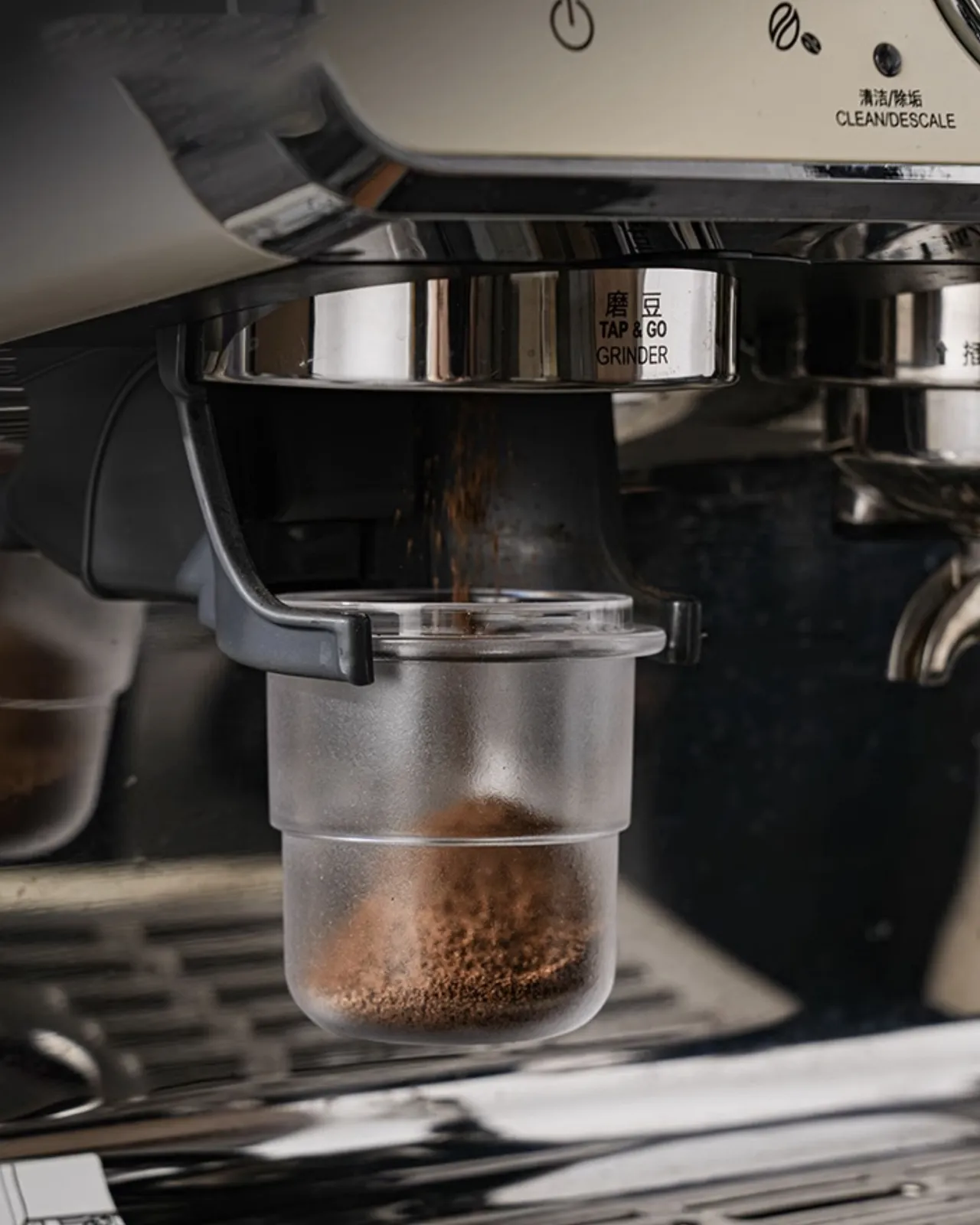 Ly dosing cup trong suốt treo trên giá đỡ máy xay cà phê, bột đang rơi từ vòi xuống ly