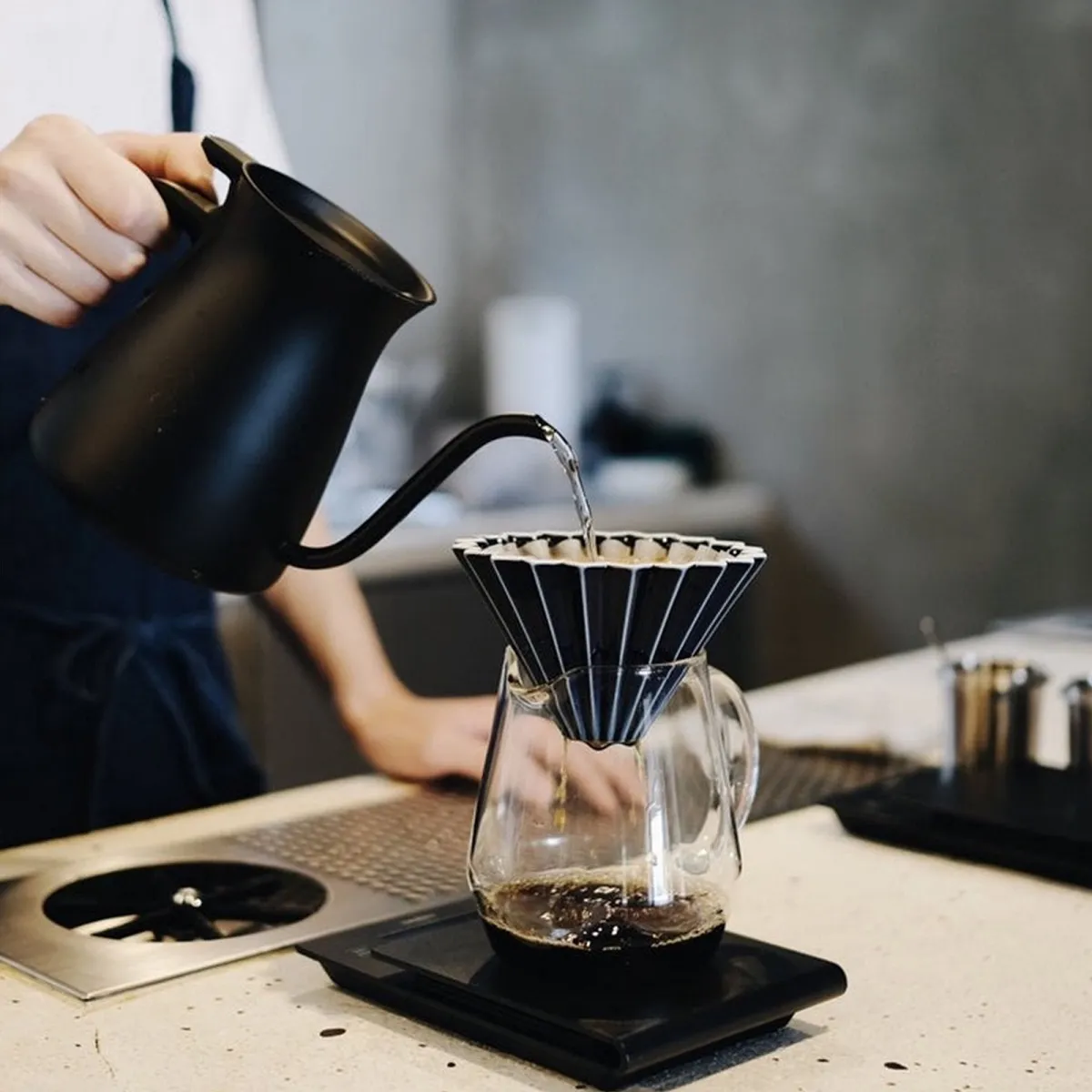 Barista rót nước bằng ấm cổ ngỗng vào phễu sứ Origami Dripper S đặt trên cân điện tử