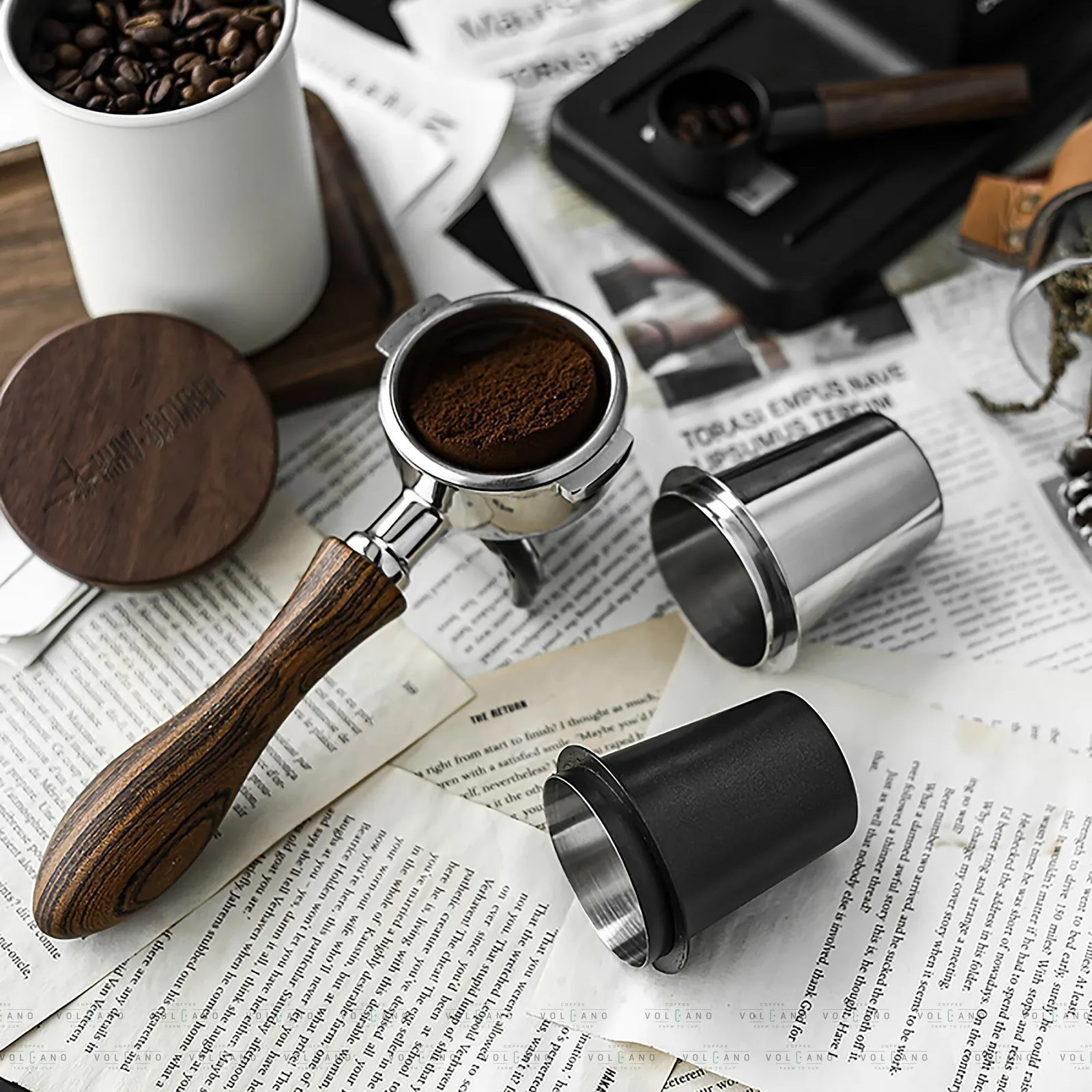 Ly dosing cup inox cùng hũ đựng cà phê và tay pha cán gỗ trên bàn