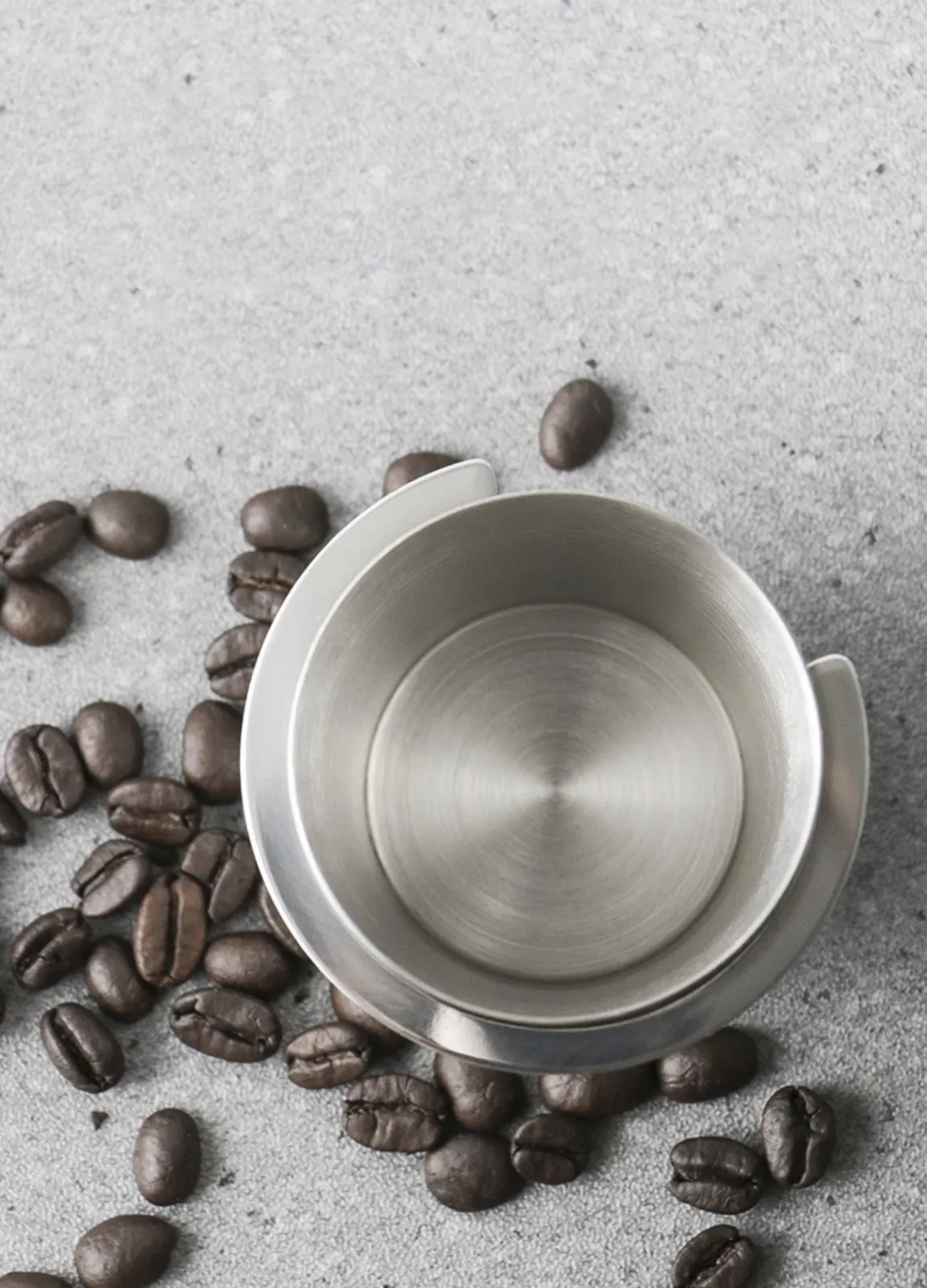 Ly dosing cup inox nằm nghiêng giữa những hạt cà phê rang