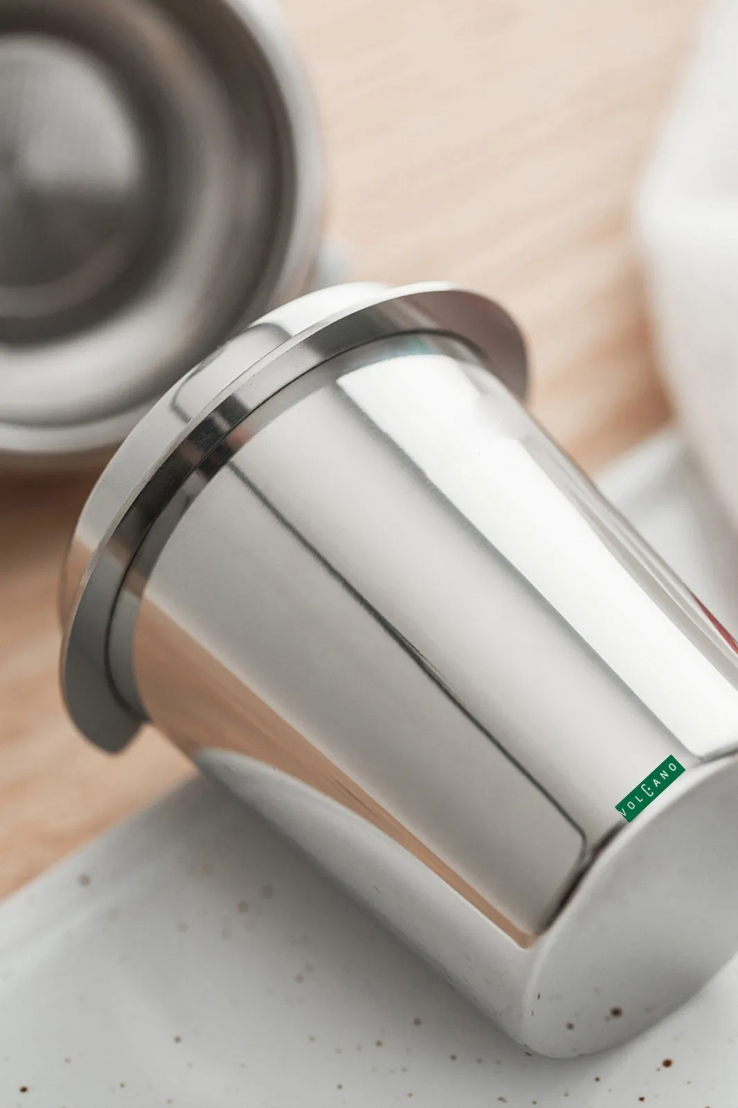 Ly dosing cup inox đặt nghiêng trên mặt bàn gỗ sáng màu