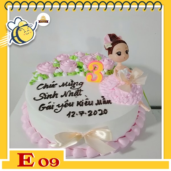 Bánh kem búp bê E09 váy hồng ngồi thẩn thơ trên nền trắng thắt nơ và hoa màu hồng nhạt dễ thương