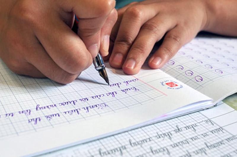 Bé lớp 2 đang viết chữ trên vở ô ly 
