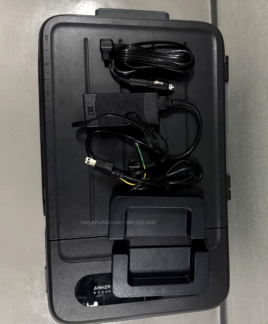 Anker A17A35A1: Dây nguồn và bộ cấp nguồn đặt trên nắp tủ.