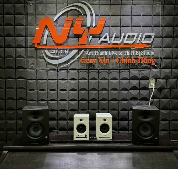 Đánh Giá Loa Kiểm Âm Ortizan C7 hình đang được chụp tại một phòng demo hoặc showroom thiết bị âm thanh, có treo logo lớn NY Audio – một đơn vị chuyên cung cấp thiết bị phòng thu và âm thanh live. Trên bức tường được xử lý tiêu âm bằng foam panel hình bán cầu, ta thấy