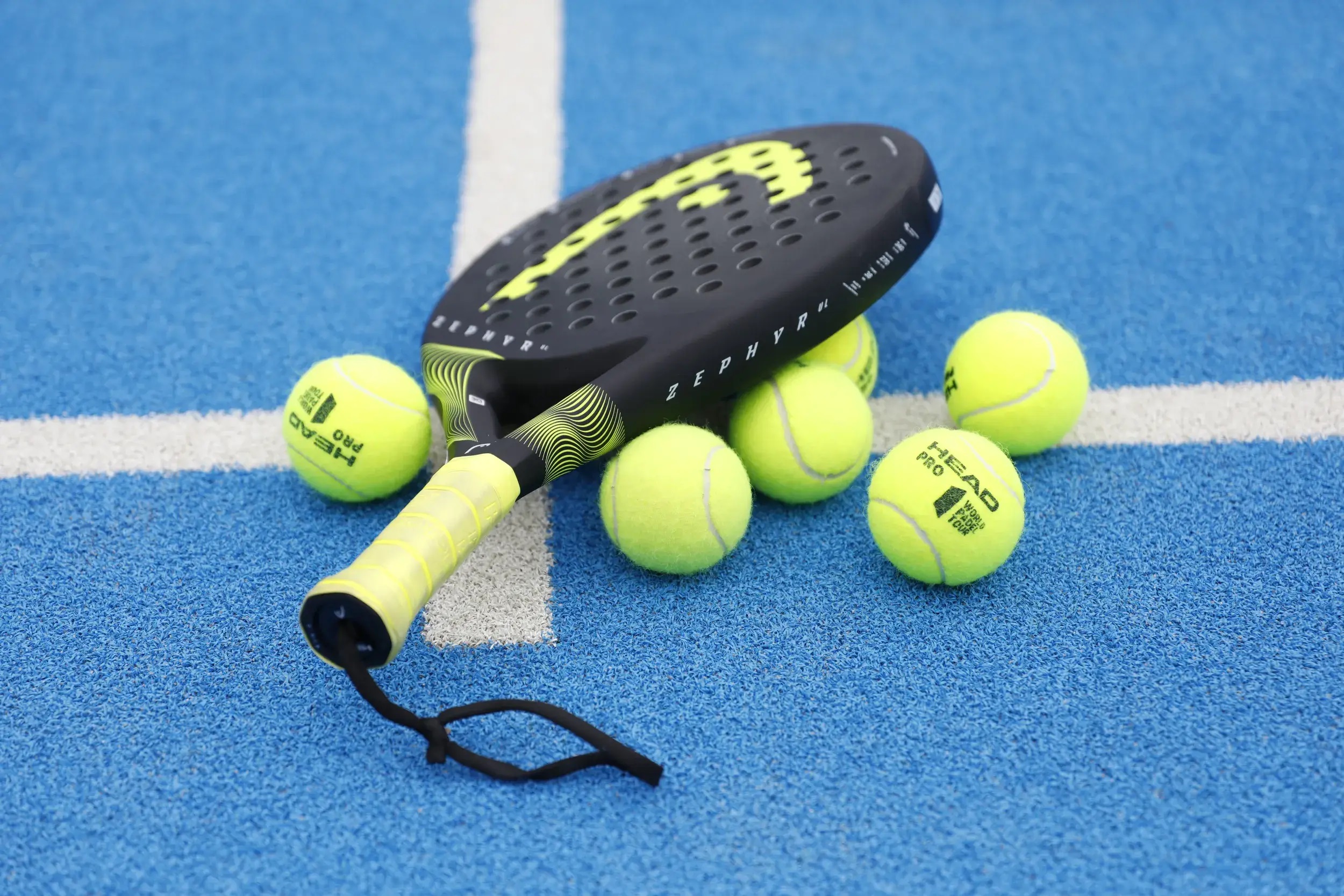 "A dynamic action shot of four athletic players engaged in a highly competitive Padel match inside a modern glass-enclosed court. The court features a vibrant blue artificial turf, surrounded by high transparent glass walls and metal mesh. The players are holding specialized padel rackets without strings, mid-swing in a dramatic pose. Bright, professional stadium LED lighting illuminating the court. The atmosphere is energetic, competitive, and modern. Cinematic lighting, hyper-realistic, 8k resolution, aspect ratio 4:3."