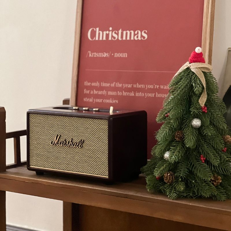 Marshall Acton III Burgundy trên kệ gỗ với backdrop Christmas poster đỏ và cây thông nhỏ