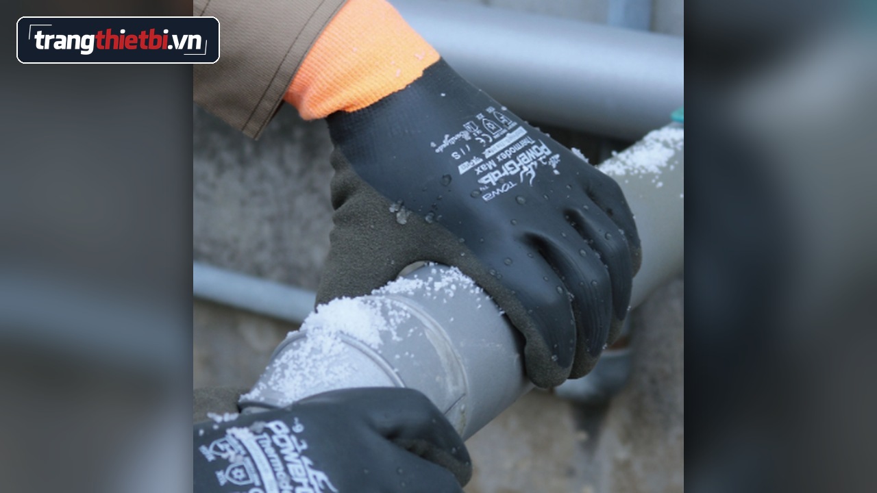 Cận cảnh đôi tay đeo găng tay chống lạnh chịu nước TOWA PowerGrab Thermo Dex Max cổ cam phủ cao su đầm nước đang bám vào đường ống dính tuyết