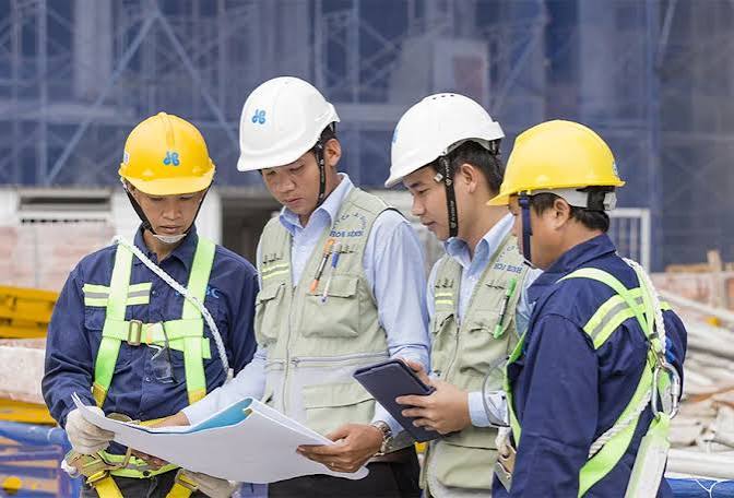 Kỹ sư và công nhân công trường đeo mũ bảo hộ dây an toàn kiểm tra bản vẽ đánh giá rủi ro