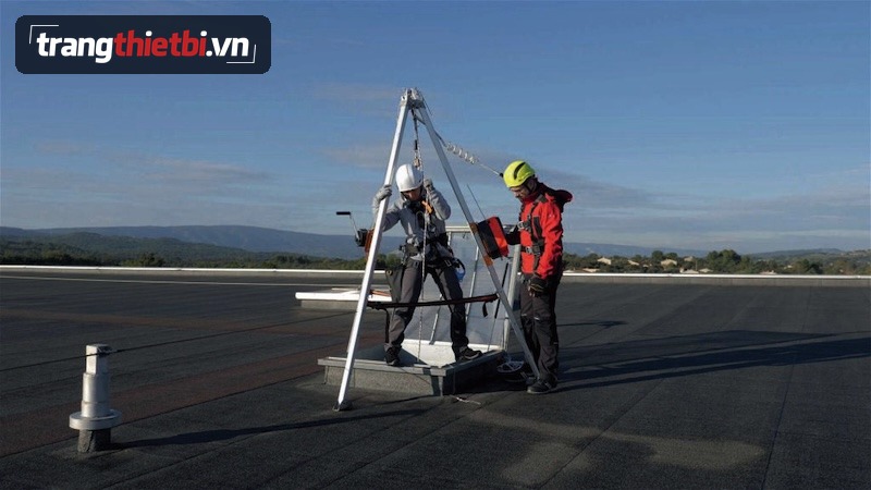Hai nhân sự an toàn đang kiểm tra vận hành giá ba chân tripod và tời hãm rơi tự động tại cửa hầm không gian hạn chế