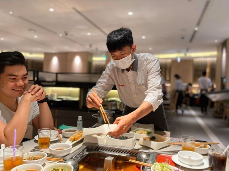 Đồng phục phục vụ Haidilao gồm sơ mi trắng cổ tàu đen, quần tối màu và tạp dề xám