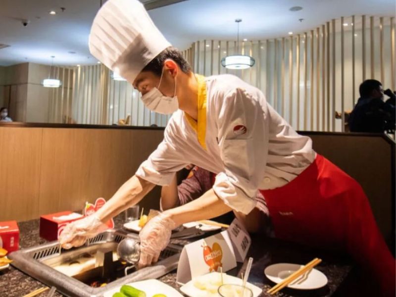 Đồng phục bếp Haidilao gồm áo cổ tàu tay ngắn, viền đỏ, hai hàng khuy và tạp dề đỏ