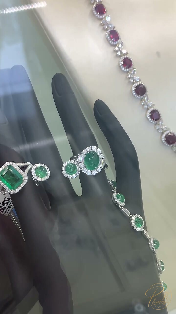 Hai nhẫn Ngọc Lục Bảo viền halo kim cương cạnh lắc tay, phía sau là vòng đính đá Garnet đỏ