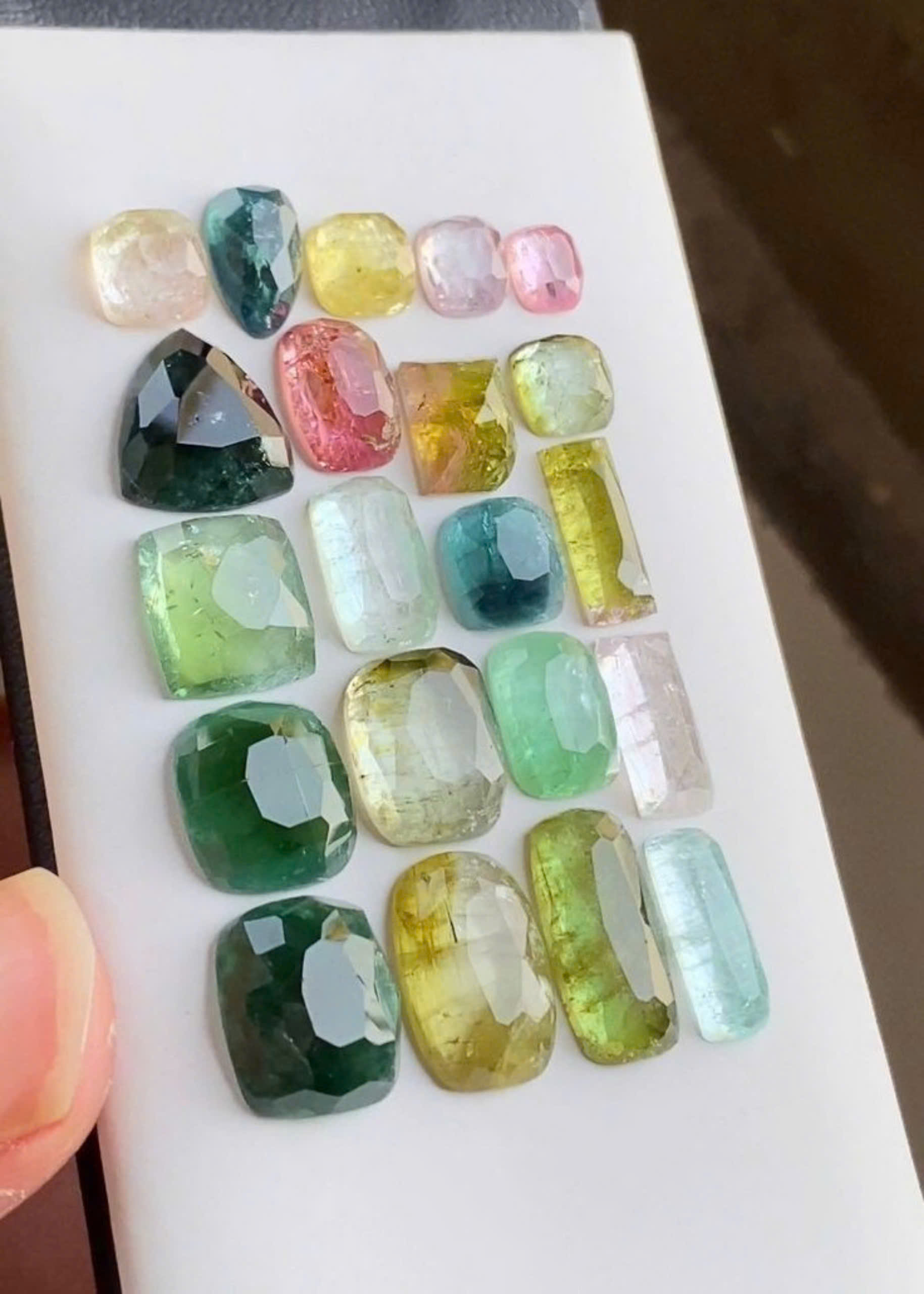 Nhiều vi&ecirc;n đ&aacute; Tourmaline đ&atilde; m&agrave;i gi&aacute;c đủ m&agrave;u hồng, lục, lam, v&agrave;ng xếp tr&ecirc;n khay trắng để so s&aacute;nh gi&aacute;