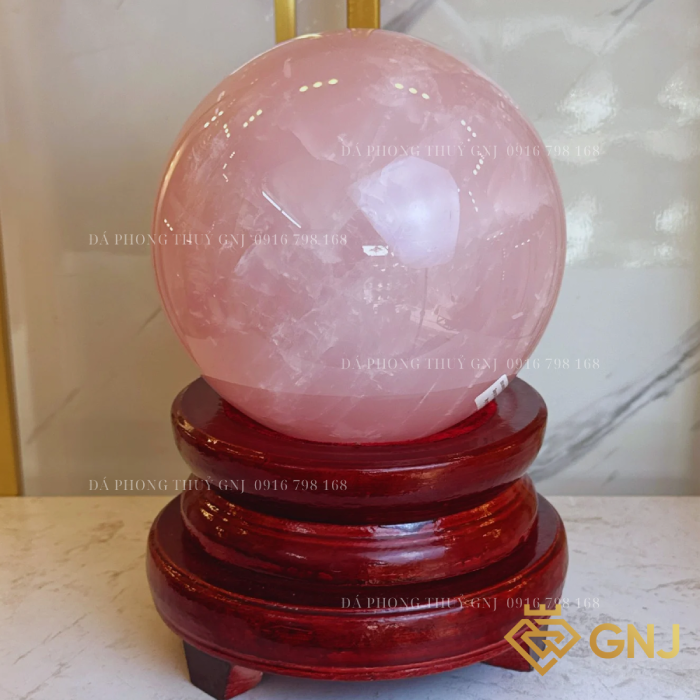 Quả Bi Cầu Đá Thạch Anh Hồng Tự Nhiên — trên đế gỗ nâu đỏ trước tủ kính