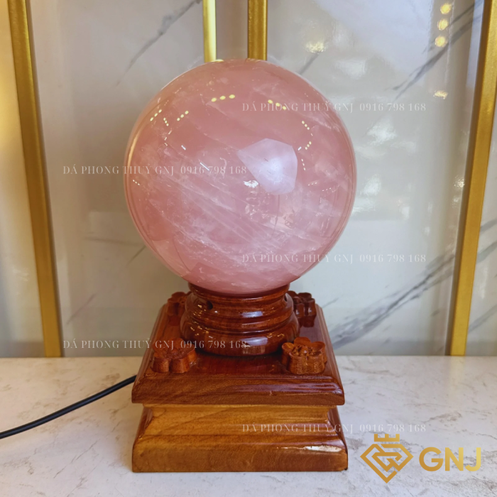 Quả Bi Cầu Đá Thạch Anh Hồng Tự Nhiên — trên đế gỗ bậc thang trước tủ kính, góc 1