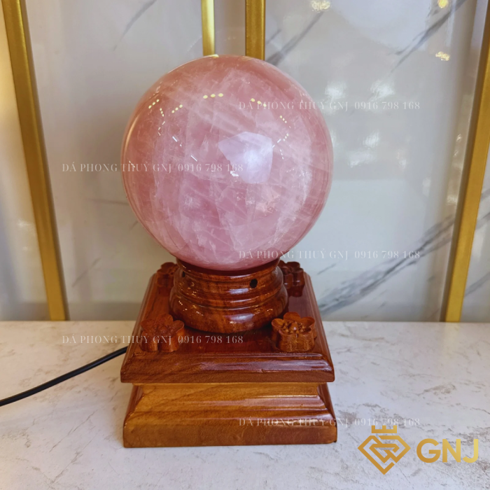 Quả Bi Cầu Đá Thạch Anh Hồng Tự Nhiên — trên đế gỗ bậc thang trước tủ kính, góc 2