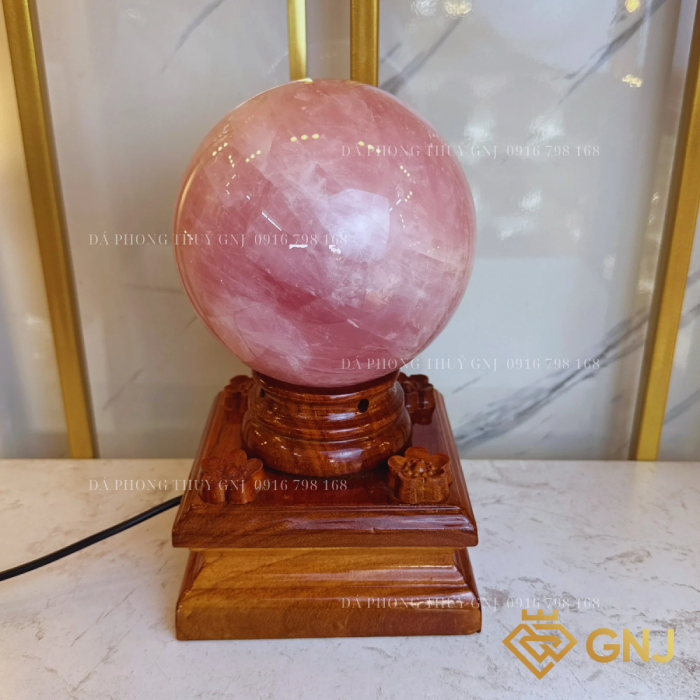 Quả Bi Cầu Đá Thạch Anh Hồng Tự Nhiên — trên đế gỗ bậc thang trước tủ kính, góc 3