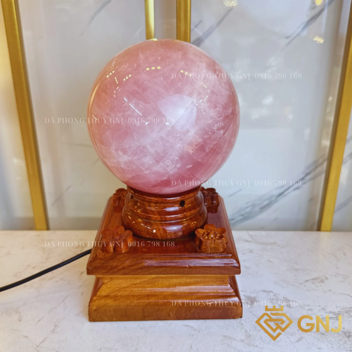 Quả Bi Cầu Đá Thạch Anh Hồng Tự Nhiên — trên đế gỗ bậc thang trước tủ kính, góc 4